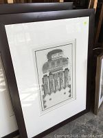 Photo showing framed architectural art print with classical elements, matted and in a scratched dark frame.