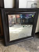 Full view of 33x33 inch square beveled mirror in dark wood frame placed on floor, showing general condition and overall design.