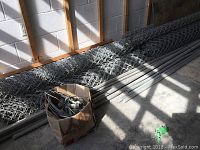 Overall view of chain link fence rolls and metal poles laid on ground in storage area