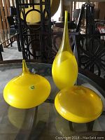 Three yellow art glass vases of varying shapes and sizes on a glass table.