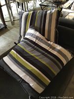 Photo showing two duck feather pillows with striped covers in grey, black, white, and olive green colors placed on a couch.