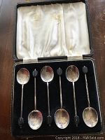 Set of six silver coffee spoons in a black velvet-lined presentation box with satin interior lid. The spoons are showing tarnish and signs of use.