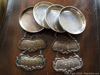 Four Gorham silver decanter tags labeled Rum, Scotch, Brandy, Gin and four round silver coasters.