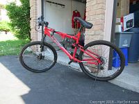 Full left-side view of red CCM full-suspension mountain bike showing frame, wheels, fork and kickstand