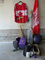 Wide view of full lot showing hockey jersey, hockey sticks, crutches, storage bags, cooler, exercise ball, and Canadian flag.