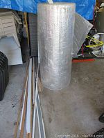 Full standing roll of reflective floor insulation next to wooden trim pieces and other items in garage.