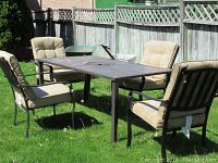Photo showing rectangular metal patio table and four arm chairs with beige cushions arranged on grass outdoors.