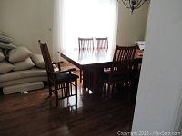 Full view of mission style dining table with 6 chairs around it in dining room. Light shining from window behind.