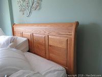 Full view of large solid oak sleigh bed headboard showing three paneled sections and curved edges.
