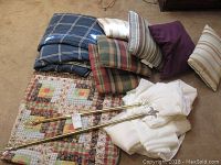 Photo showing folded log cabin quilt, assorted decorative pillows with striped and plaid patterns, sheer white curtains, and two decorative metal curtain rods with ornate finials.
