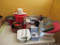 Mixed kitchen items grouped on corner shelf including Rival appliances, punch bowl, wooden bowls, plastic storage containers, metal water bottles