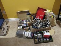 Photo displaying assorted cables, disc storage items, boxes of light bulbs, and a projection clock radio.