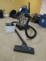 Full view of Vacmaster vacuum with attached hose, floor cleaner head, and additional accessories on carpeted floor.