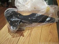 Small black kayak propeller still in plastic wrap with bubble wrap underneath on wooden surface.