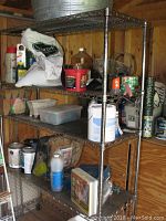 Full view of the shelving unit showing four wire shelves with assorted items stored on them, standing inside a wooden shed or storage area.