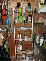 Full view of white metal over-the-door rack with multiple shelves holding assorted bottles and cans, including garden and cleaning supplies. Rack shows wear and is placed against wooden wall in a shed.