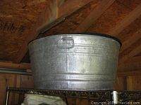 Side view of galvanized tin tub showing metal handle, dents, and surface wear