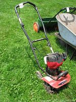 Full view of Troy Bilt tiller standing on grass, showing handlebar, engine, and wheels.