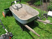 Side view of heavy duty steel wheelbarrow showing large tub and black handles on grass