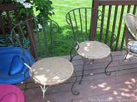 Two wicker seated metal framed chairs on a wooden deck with lawn and garden hose visible in background.