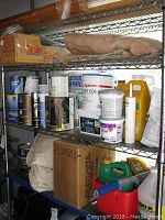 Metal shelving with various plumbing and paint supplies including buckets, cans, and boxes