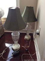 Two clear glass base table lamps with round brass-tone pedestals and large fabric shades.