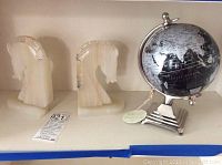 Photo showing two alabaster horse head bookends and a silver and black decorative globe on a white shelf.