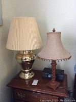 Photo showing both table lamps on a wooden dresser; brass lamp with pleated shade and wooden lamp with woven beaded shade, with iHome docking station visible below lamps.