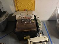 Overview photo showing sewing machine, wood care system box, and craft supplies in containers.