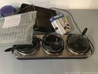 Triple Crock-Pot slow cooker with three pots, spoons, and additional cookware and accessories including a baking tray and large pot with lid.