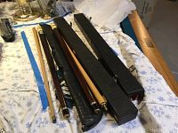 Lot contents, three pool cues laid side-by-side on a surface alongside two black hard cases and one black leather soft case.