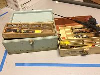 Two fishing tackle boxes, one vintage metal and one plastic Plano, showing various fishing supplies including fishing lures and hooks.