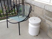Metal patio chair with blue elastic cords and white decorative piece on a concrete patio near a brick wall and railing.