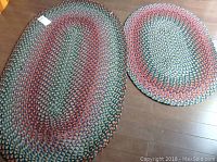 Two oval braided rugs laid on the floor, showing distinct multicolor concentric braided patterns.