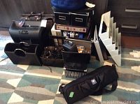 Lot overview showing Staples shredder, briefcase, tripod bag, binders, magazine rack, and other office supplies on a floor with striped rug.