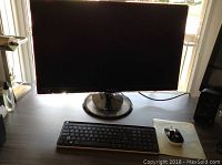Samsung 27 inch widescreen monitor on desk, black finish, round stand base, wired connection visible
