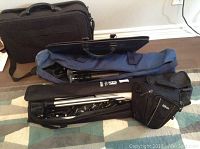 Full view of all items showing tripod, photo umbrella with bag, Nikon camera case, and parts of briefcase and portfolio case.