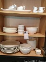 Shelves showing stacked large and small white plates, bowls, gravy boats, and small sauce bowls.