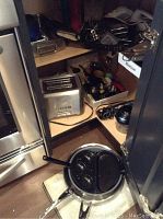 Various kitchen items and appliances stored inside a cabinet including toaster, utensils, pans, measuring cups, and several kitchen tools.