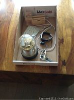 Photo of lot contents inside a cardboard box: barometer in glass dome, wood dock station with USB cord, Swiss Army knife, decals, Microsoft Band and wire.