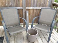 Pair of metal frame patio chairs with mesh seats and backs on a wooden deck, with plastic planter pot placed between them and BBQ mat rolled up behind.