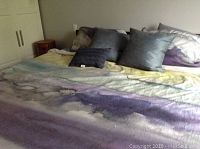 Bed made with multicolored linens and several pillows with various shades of blue and purple.
