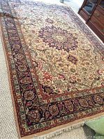 Full view of the area rug showcasing central medallion and floral border design in red, navy blue, cream, and green hues.