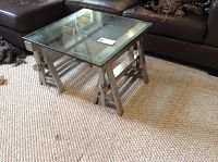 Glass coffee table with metal base on carpet, showing overall structure and glass top.