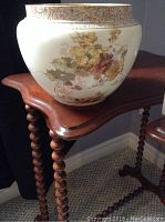 Side view of the large ceramic planter showing leaf pattern while sitting on wooden furniture with spool legs.
