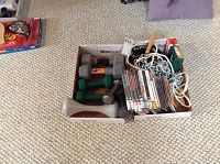 Wide view showing the collection of hand weights, DVDs, CD, skipping rope box, and bike chain arranged in two cardboard boxes on carpeted floor.