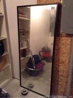 Front view of the tall rectangular mirror leaning against wall near shelves and utility panel.