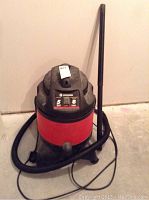 Full view of King Canada wet-dry vacuum, red and black with hose and wand attached.