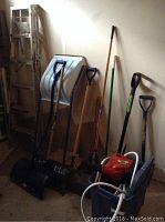Photo showing wooden step ladder, multiple shovels, garden rake, Fiskars electric blower, and Black & Decker cordless broom with charger