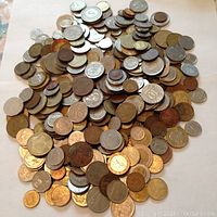 Photo showing a pile of mixed world coins from different years and denominations on white background. Coins vary in size, color, and metal composition.